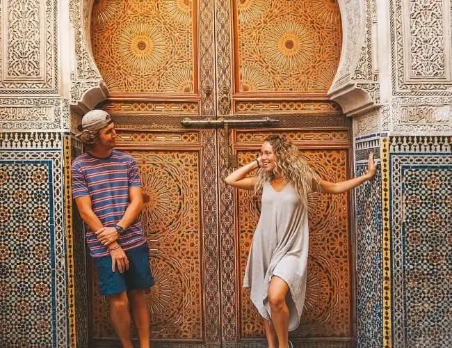 Two travellers in front of a carved wooden door